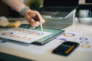 Eine Hand zeigt auf Diagramme und Grafiken auf einem Tablet, um Finanzdaten zu analysieren.