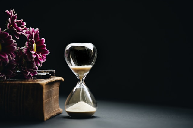 Sanduhr neben einem alten Buch und Blumen – Symbol für Zeit, Wissen und wertvolle Entscheidungen im Immobilienmarkt.