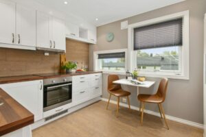 Moderne Küche mit weißen Schränken, Holzarbeitsfläche und braunen Stühlen, ideal für ein gemütliches Esszimmer.