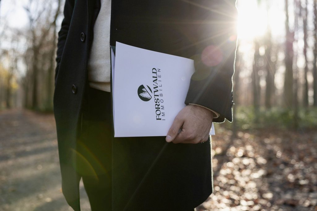 Forstwald Immobilien – Detailaufnahme einer Immobilienmappe in der Hand eines Maklers mit Sonnenlicht im Hintergrund.