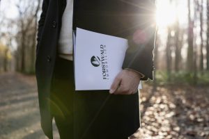 Forstwald Immobilien – Detailaufnahme einer Immobilienmappe in der Hand eines Maklers mit Sonnenlicht im Hintergrund.